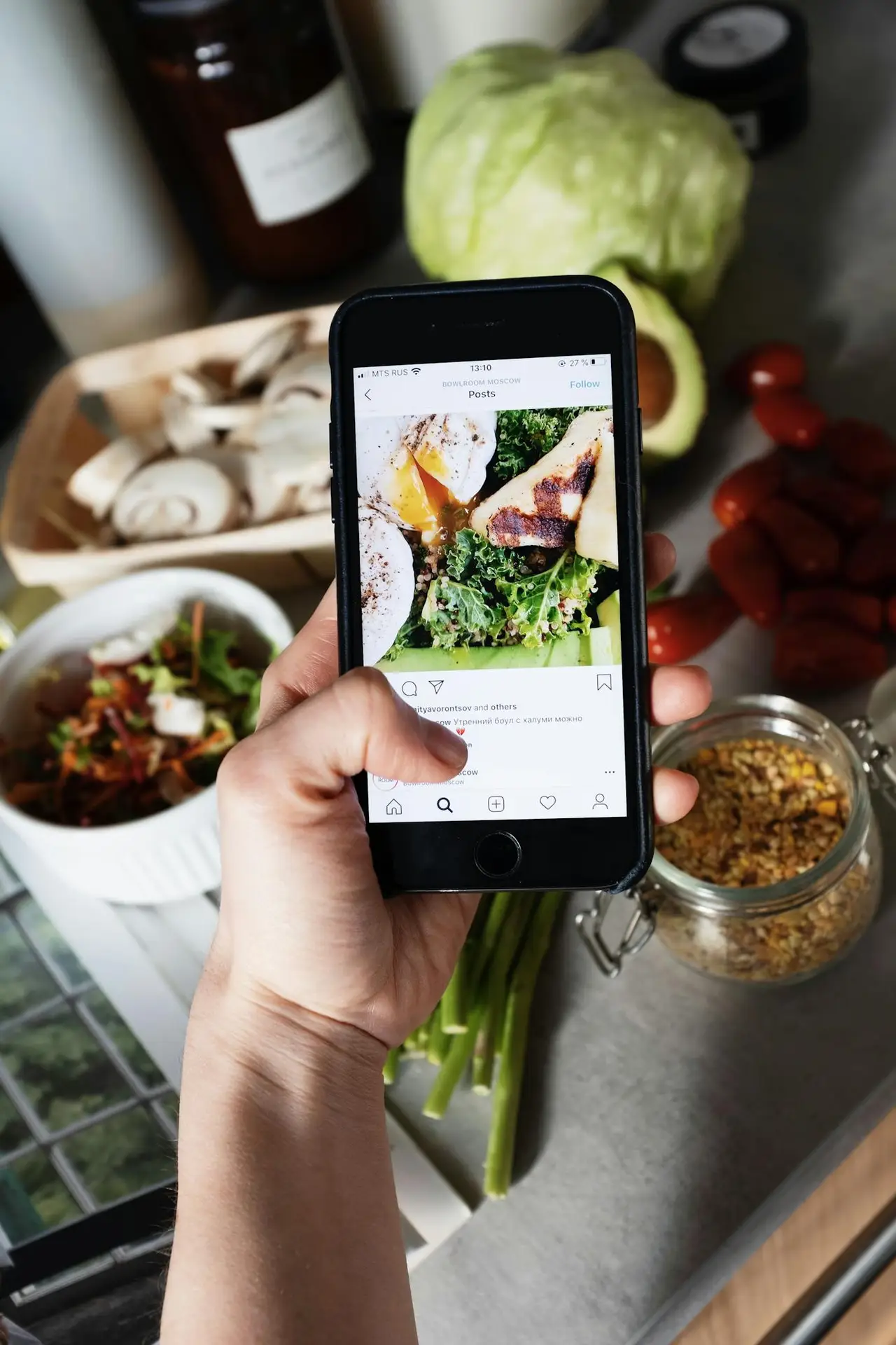 From above of crop person touching cellphone screen while searching for image of healthy recipe and standing in kitchen in front of vegetables